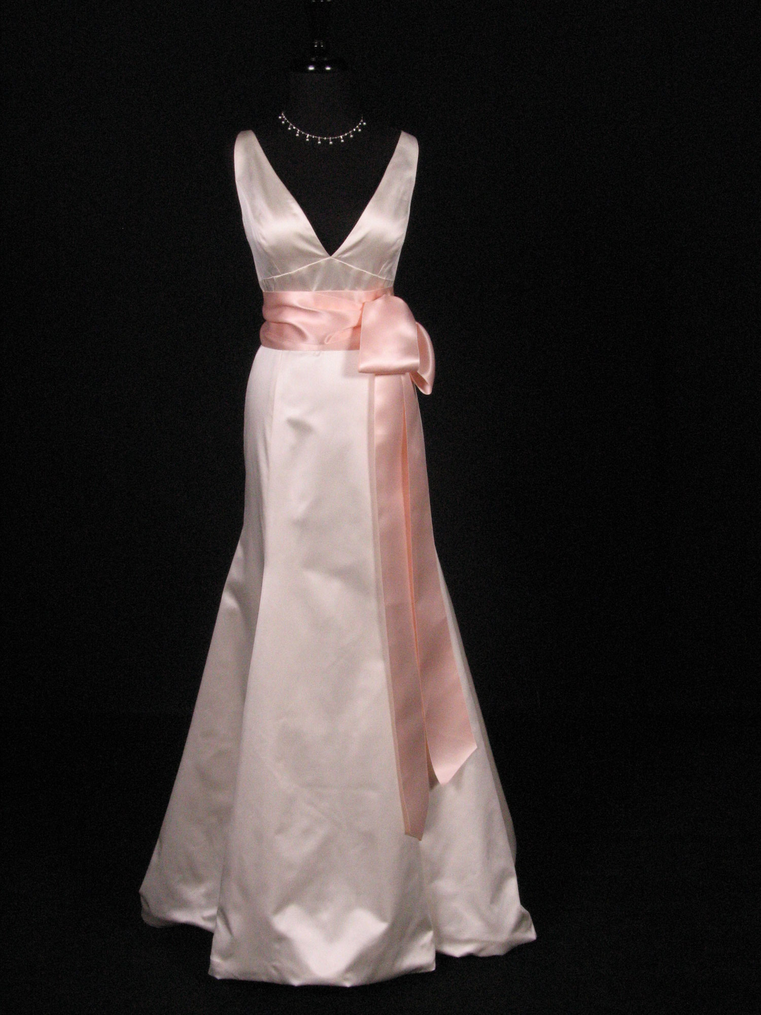 Wedding dress on a form with a light peach satin ribbon sash