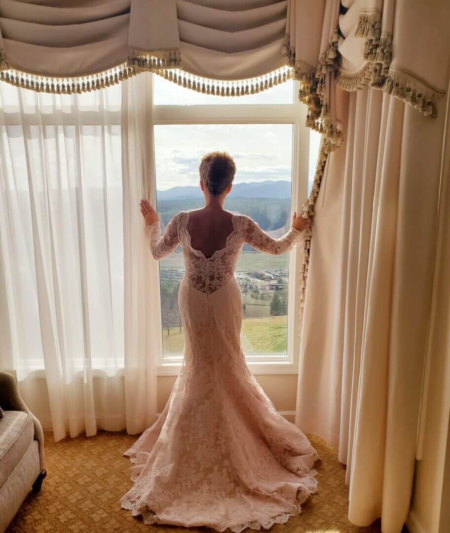 Bride in a fitted lace gown at a draped window, back view